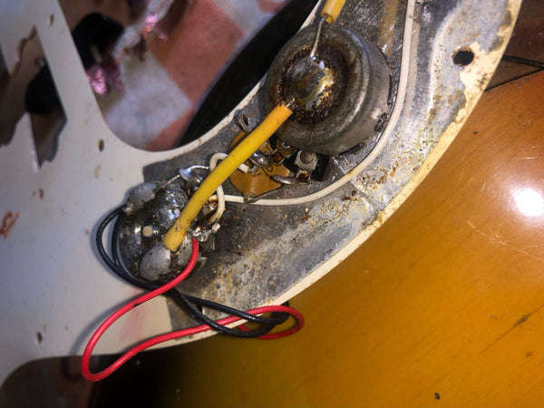 Close-up of vintage electric guitar wiring showing potentiometers, wires, and aged metal components inside guitar body cavity
