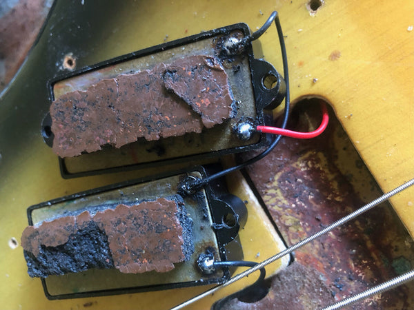 Close-up of vintage electric guitar pickups with aged and corroded copper shielding tape and exposed wiring inside the guitar body cavity