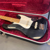 Black vintage electric bass guitar with maple fretboard and white pickguard in open red velvet-lined hard case