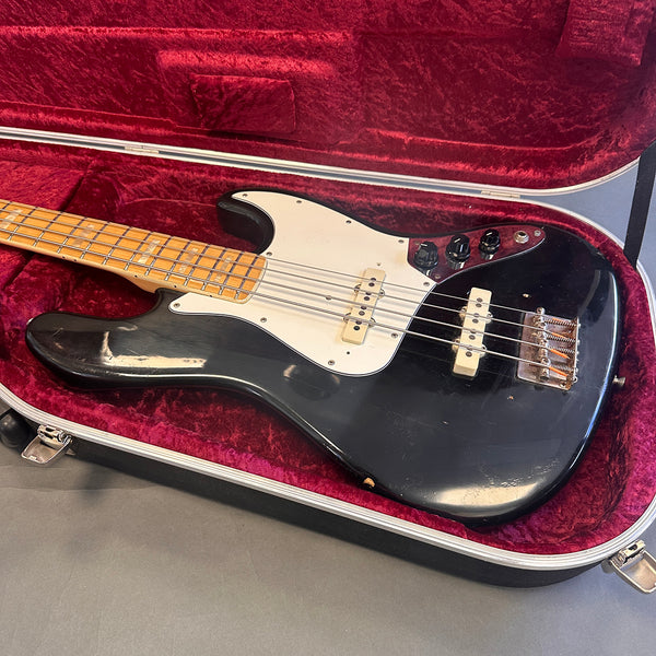 Black vintage electric bass guitar with maple fretboard and white pickguard in open red velvet-lined hard case