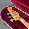 Fender Jazz Bass headstock with tuning pegs inside red velvet-lined hard case, close-up view of maple neck and logo on wood grain