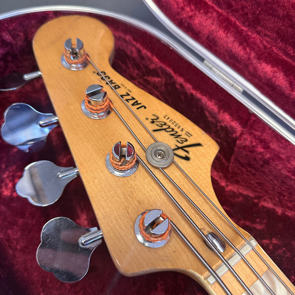 Close-up of Fender Jazz Bass headstock with tuning pegs and strings in plush red case interior