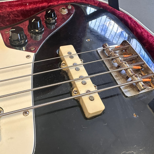 Close-up of black electric bass guitar showing pickup, bridge, and control knobs inside a red velvet-lined guitar case.