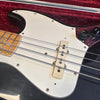Close-up of black electric bass guitar body with white pickguard, chrome strings, maple fretboard, and black control knobs in a red velvet-lined case