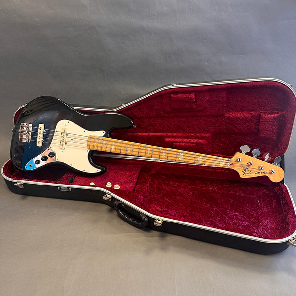 Vintage Fender Jazz Bass guitar in black finish with maple neck, shown inside a red velvet-lined hard case, four metal tuning pegs visible on headstock.