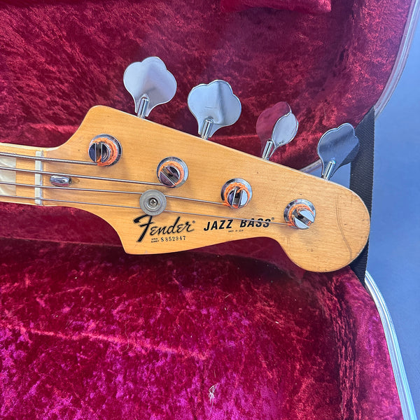 Close-up of Fender Jazz Bass headstock with tuning pegs and strings against red velvet guitar case lining