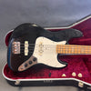 Black vintage electric bass guitar with white pickguard and maple neck resting in red velvet lined Hiscox hard case on gray background