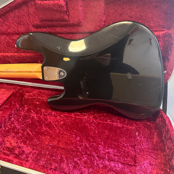 Black electric guitar body with visible wear and scratches on a red velvet-lined case interior, showing the neck plate with Fender logo.