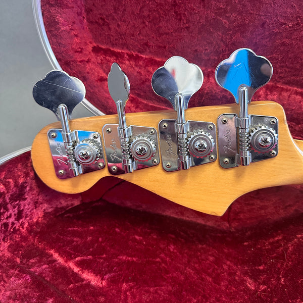 Close-up of chrome Fender bass guitar tuning pegs on maple headstock inside red velvet guitar case
