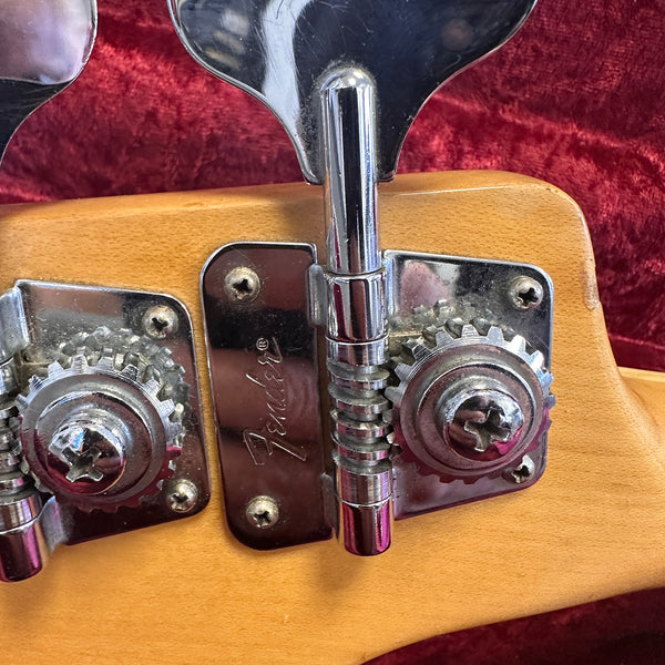 Close-up of chrome tuning pegs on a Fender guitar headstock with natural wood finish and red velvet background