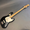 Black Fender Jazz Bass guitar with maple neck and white pickguard lying on gray surface