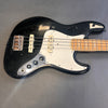 Black electric bass guitar with white pickguard and maple fretboard on gray background, vintage style instrument with four strings and chrome tuning knobs.