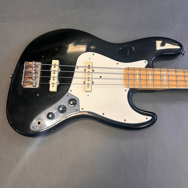 Black electric bass guitar with white pickguard and maple fretboard on gray background, vintage style instrument with four strings and chrome tuning knobs.