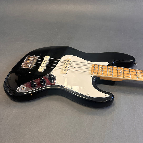 Black electric bass guitar with white pickguard and maple fretboard on gray background