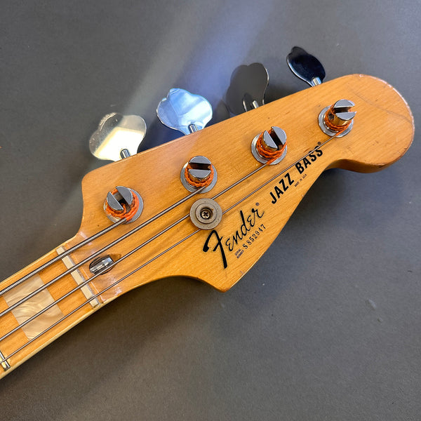 Close-up of natural wood Fender Jazz Bass guitar headstock with tuning pegs and strings on gray background