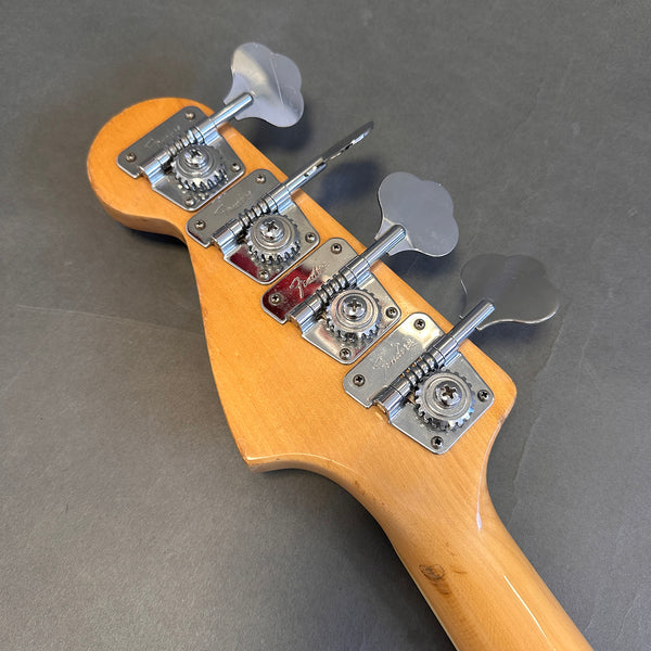 Fender bass guitar headstock with four vintage-style chrome tuning pegs on natural wood finish against gray background