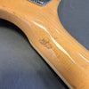 Close-up of natural wood guitar neck with visible dent and scratch on the back, showing wear and finish details against a gray background