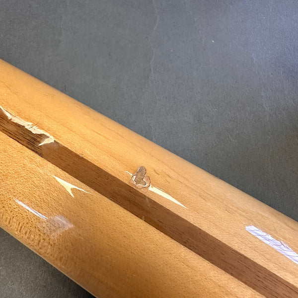 Close-up of guitar neck with visible chips and dents in the wood finish on a light brown wooden surface
