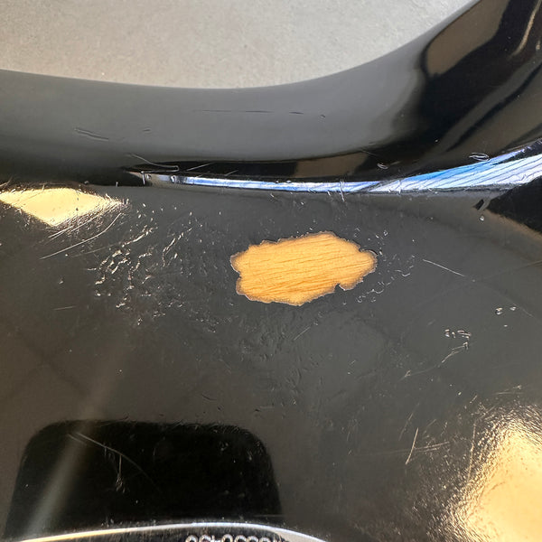 Close-up of black electric guitar body with visible paint chip and surface scratches showing wood underneath