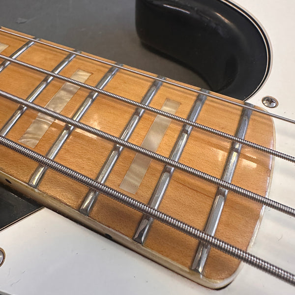 Close-up of maple guitar fretboard with metal frets and pearl rectangular inlays on electric bass guitar strings and white guitar body
