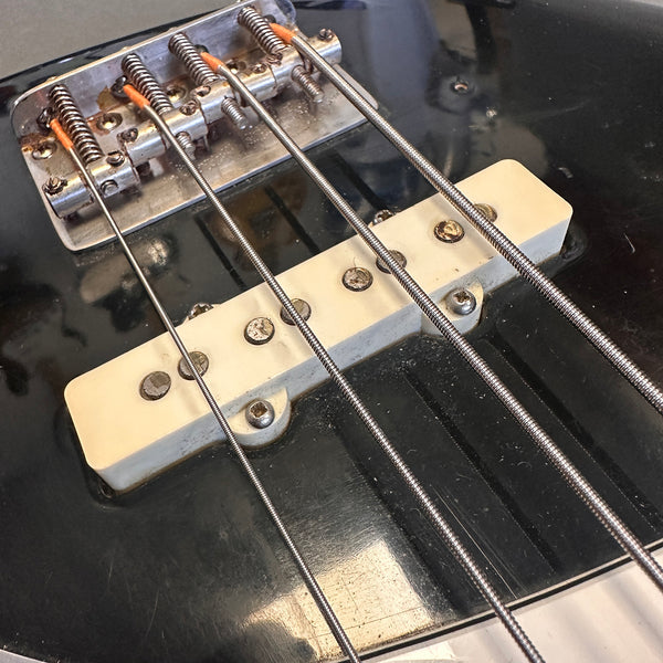 Close-up of black electric bass guitar bridge and white pickup with metal strings and adjustable saddles