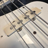 Close-up of white single-coil pickup and steel strings on electric bass guitar body with worn finish and visible screws