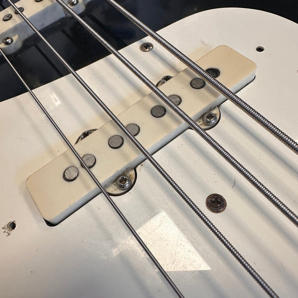 Close-up of white single-coil pickup and steel strings on electric bass guitar body with worn finish and visible screws
