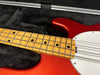 Close-up of maple fingerboard and red electric bass guitar body with white pickguard inside black plush case with bow accessory.