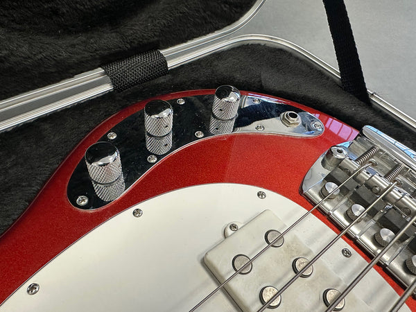 Close-up of red electric bass guitar control knobs, pickup, and bridge inside a black padded guitar case