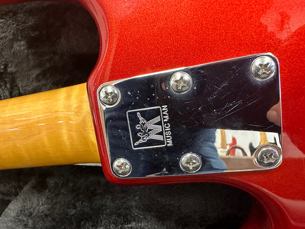 Close-up of Music Man guitar neck plate with screws on red electric guitar body and maple neck on black fabric background