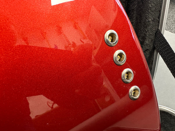 Close-up of red electric guitar body showing four string ferrules and glossy metallic finish