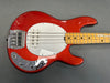 Red electric bass guitar with white pickguard and maple neck on gray surface