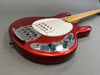 Close-up of red electric bass guitar body with white pickguard, chrome bridge, and control knobs on gray background