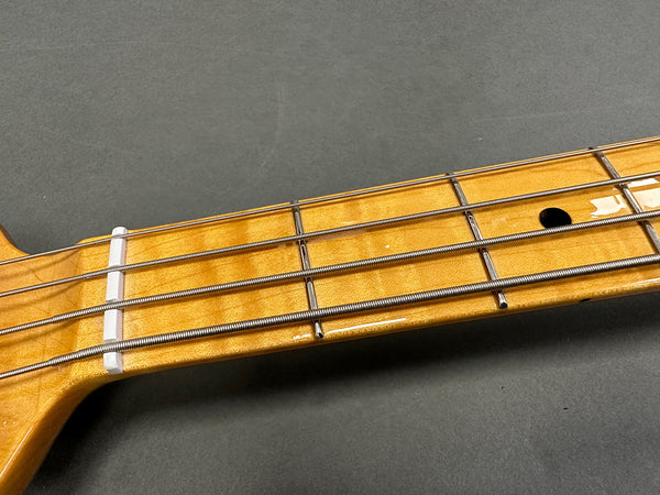 Close-up of maple bass guitar neck and fretboard with metal frets and wrapped bass strings on gray background