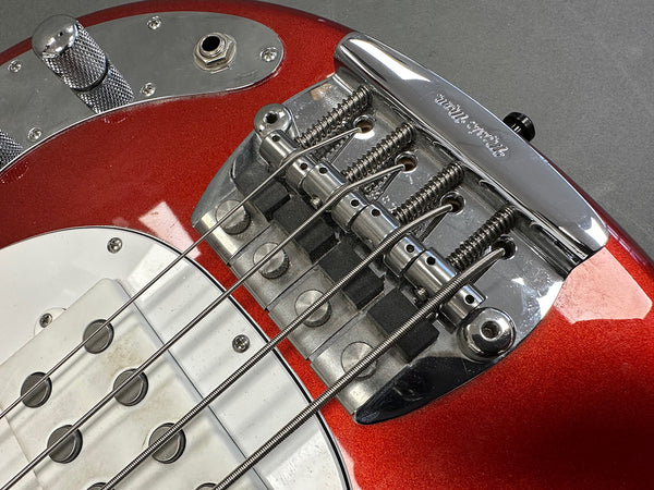 Close-up of red electric bass guitar bridge and strings with white pickup and chrome control plate on gray background