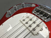 Close up of red electric bass guitar body showing white pickguard, chrome bridge, pickups, and control knobs