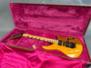 Yellow electric guitar with black pickups and triangle inlays inside pink velvet-lined guitar case with guitar pick.