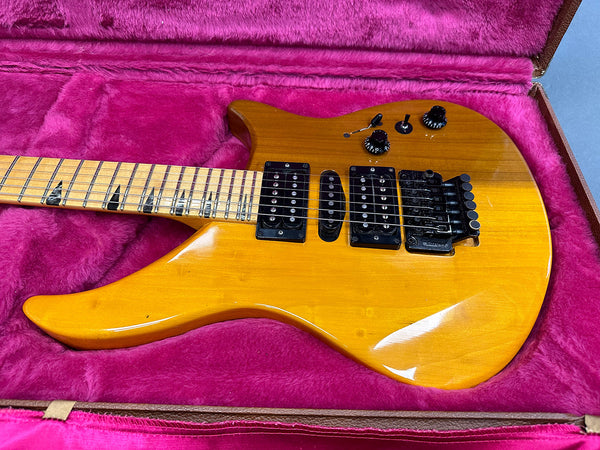 Electric guitar with yellow finish, dual humbucker pickups and single coil pickup, Floyd Rose tremolo bridge, and maple fretboard with black triangle inlays, displayed in pink plush-lined guitar case