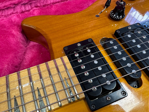 Close-up of honey burst electric guitar body and maple neck with black humbucker pickups and tone control knob on pink plush background