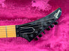 Close-up of black Gibson electric guitar headstock with six tuning pegs and strings, on bright pink plush background