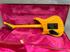 Back view of honey-colored electric guitar with black backplates inside pink plush-lined guitar case with guitar pick.