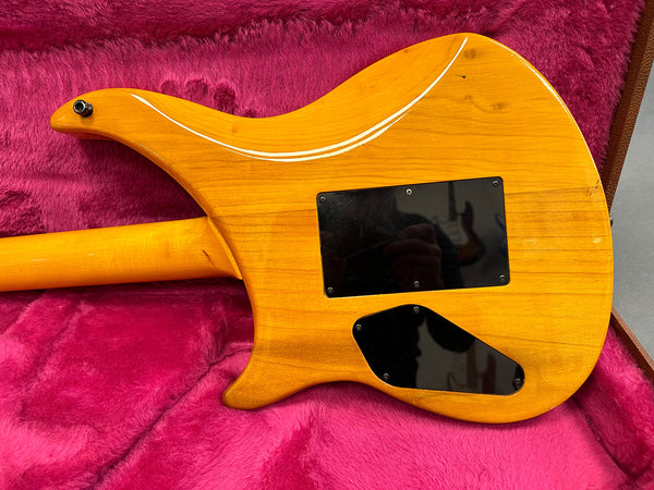 Back view of orange electric guitar body with two black plastic cover plates, resting on a pink plush guitar case interior