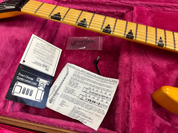 Guitar neck with black triangular inlays resting on pink plush interior with instruction manuals and hex keys for Front Change Combination Lock and Gibson M-III Standard & Deluxe engineering data sheet