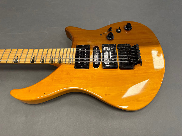 Electric guitar with natural wood finish, black pickups, two control knobs, and Floyd Rose tremolo system on gray background