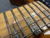 Close-up of guitar fretboard with metal frets and strings on light wood neck with pearloid inlays