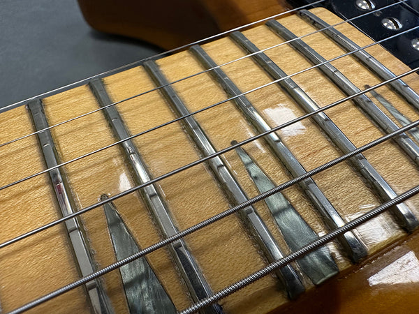 Close-up of guitar fretboard with metal frets and strings on light wood neck with pearloid inlays