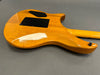 Back of natural wood electric guitar body with black plastic covers and strap button on gray surface