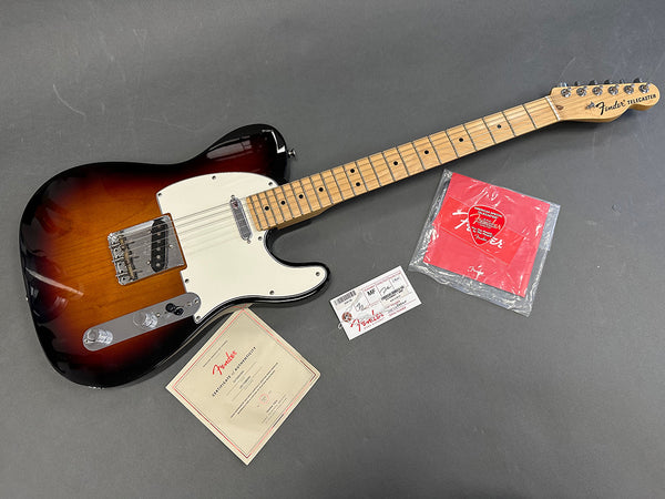Fender Telecaster electric guitar in sunburst finish with maple neck, white pickguard, Fender certificate of authenticity, tags, and Fender guitar picks on gray background.