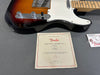 Fender electric guitar body close-up with certificate of authenticity and Fender hang tag on gray surface