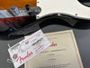Close-up of Fender guitar control knobs, assembly tag, and certificate of authenticity with serial number and model details.